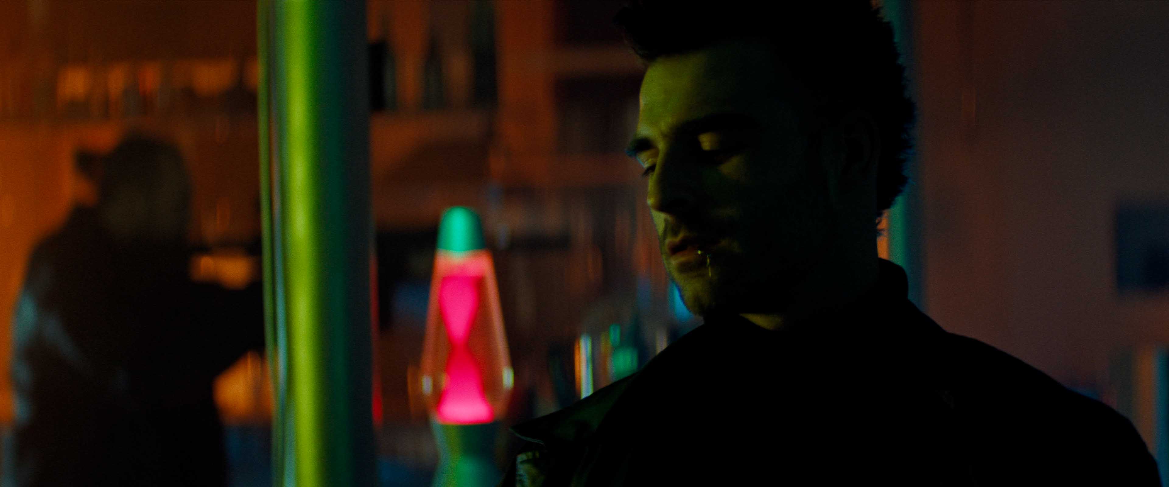 Aerial view of an alpine lakeside road with avalanche gallery; tiny sports car speeds along the shoreline.