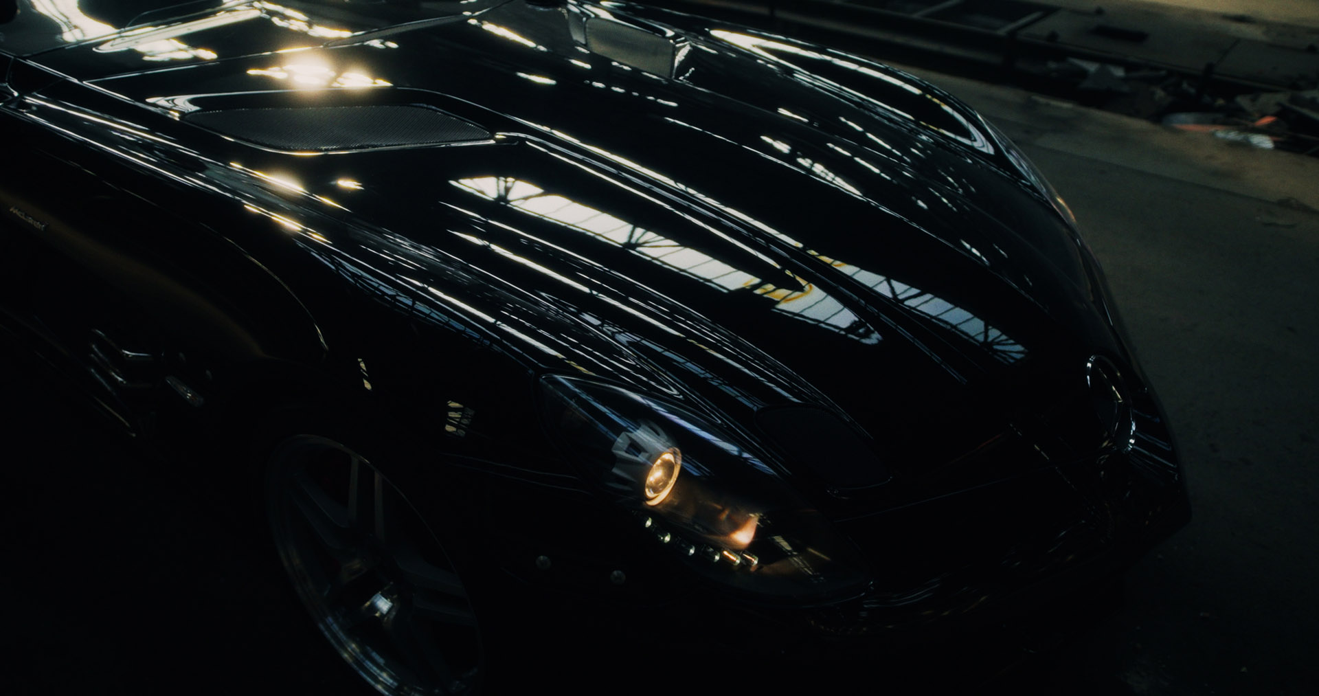 Aerial view of an alpine lakeside road with avalanche gallery; tiny sports car speeds along the shoreline.