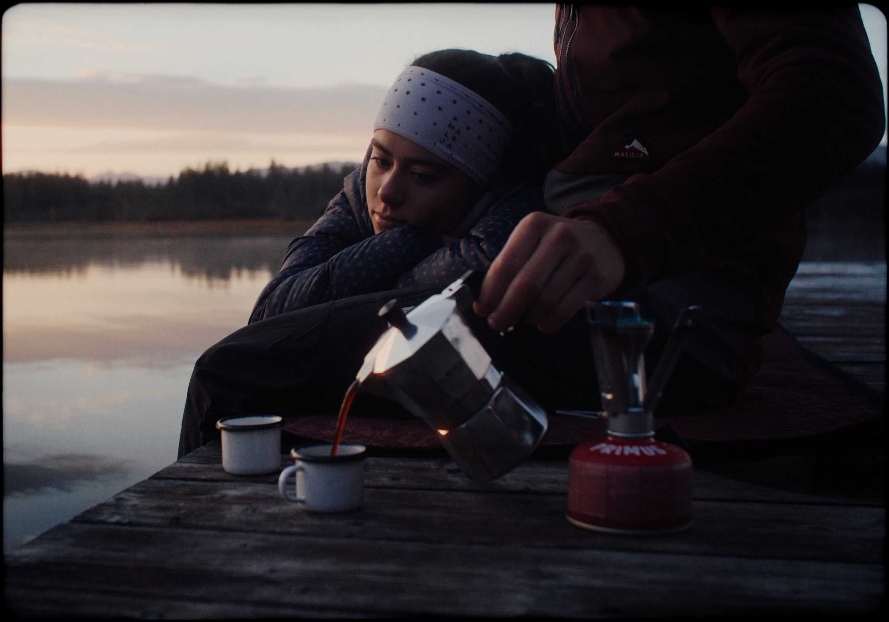 Silhouette of a helmeted racing driver at dusk, mountain skyline faintly visible under violet sky.